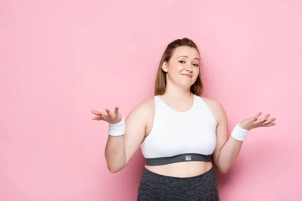 Confused overweight girl in sportswear showing shrug gesture on pink — Stock Photo
