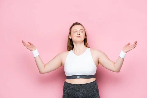 Smiling overweight girl in sportswear standing with open arms on pink — Stock Photo