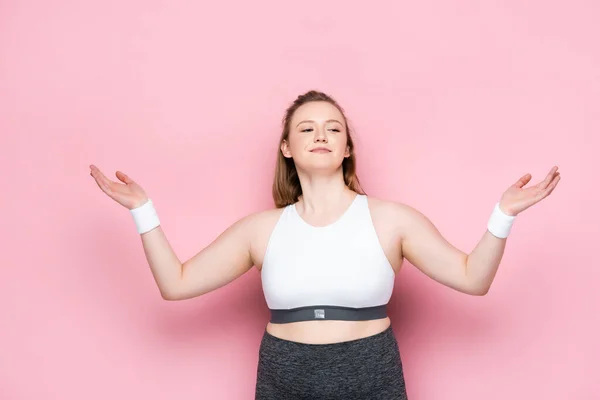 Sonriente chica con sobrepeso en ropa deportiva de pie con los brazos abiertos en rosa - foto de stock