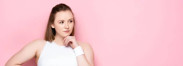 Horizontal image of pensive overweight girl touching chin and looking away on pink — Stock Photo