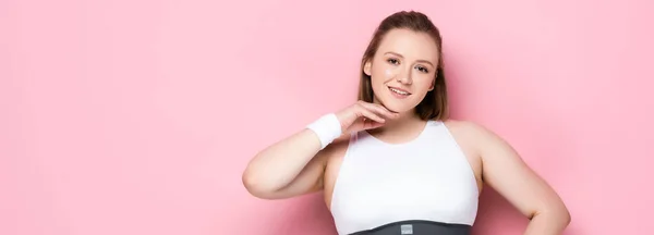 Panoramic shot of pretty overweight girl touching chin and looking at camera on pink — Stock Photo
