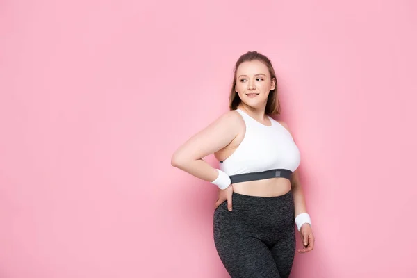 Hübsches, lächelndes übergewichtiges Mädchen, das mit der Hand auf der Hüfte auf rosa steht — Stockfoto