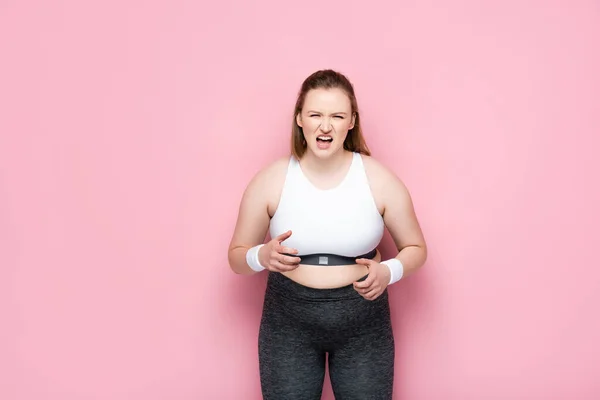 Irritated overweight girl in sportswear screaming on pink — Stock Photo