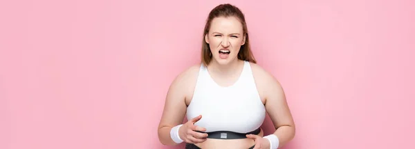 Imagen horizontal de chica enojada con sobrepeso en ropa deportiva gritando en rosa - foto de stock