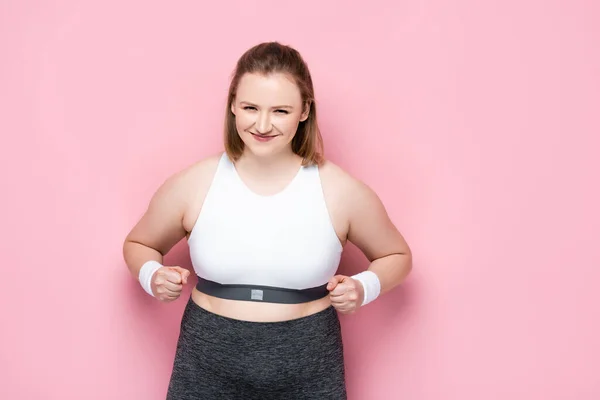 Excitada chica con sobrepeso mostrando el gesto ganador en rosa - foto de stock