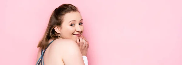 Imagen horizontal de alegre chica con sobrepeso tocando la barbilla mientras mira a la cámara en rosa - foto de stock