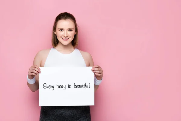 Happy overweight girl holding placard with every body is beautiful inscription on pink — Stock Photo