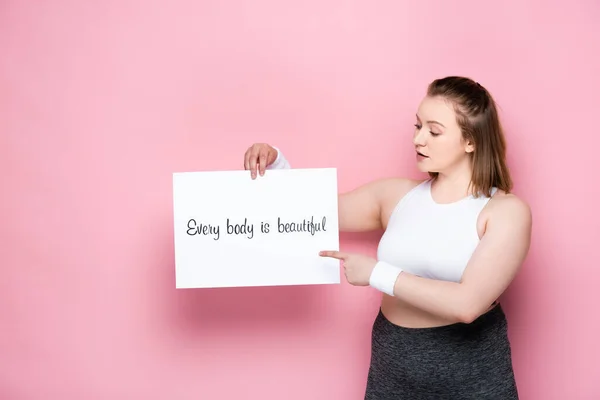 Pretty overweight pointing at placard with every body is beautiful inscription on pink — Stock Photo