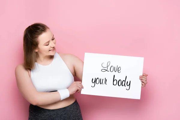 Felice ragazza in sovrappeso che tiene cartello con amore la tua iscrizione del corpo su rosa — Foto stock