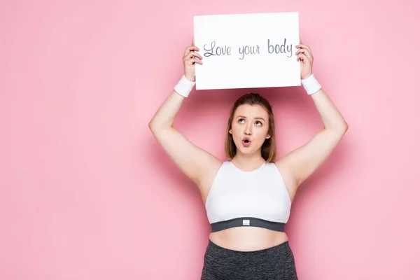 Excited overweight girl holding placard with love your body inscription above head on pink — Stock Photo