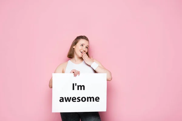 Flirty overweight girl holding placard with I am awesome inscription on pink — Stock Photo