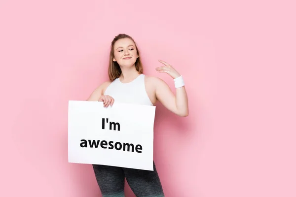 Happy overweight girl holding placard with i am awesome inscription on pink — Stock Photo