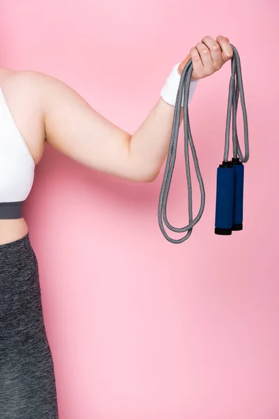 Cropped view of overweight girl holding jumping rope on pink — Stock Photo