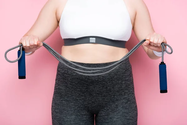Vista parcial de chica con sobrepeso en ropa deportiva sosteniendo la cuerda de salto en rosa - foto de stock