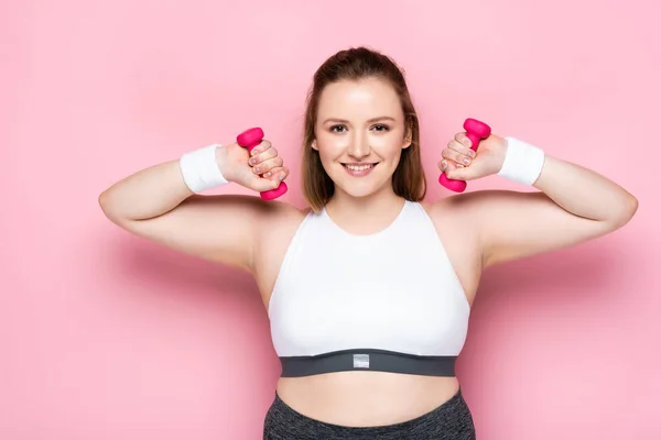 Grazioso plus size ragazza formazione con manubri sorridendo alla fotocamera su rosa — Foto stock