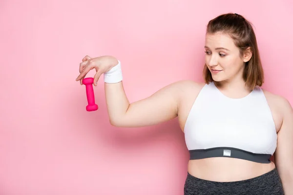 Smiling overweight girl holding dumbbell on pink — Stock Photo