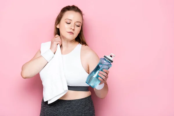 Chica atractiva con sobrepeso limpiando con toalla blanca mientras sostiene la botella de deportes en rosa - foto de stock
