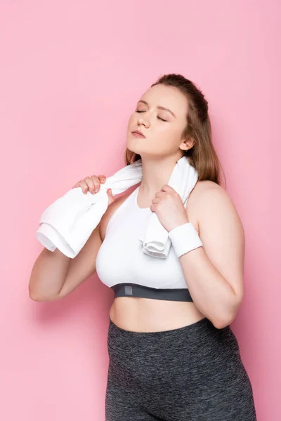 Chica bastante obesa con los ojos cerrados limpiando el cuello con toalla blanca en rosa - foto de stock