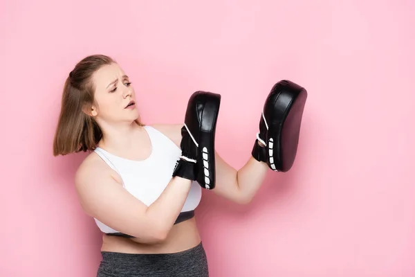 Scared size plus girl training in boxing pards on pink — Stock Photo