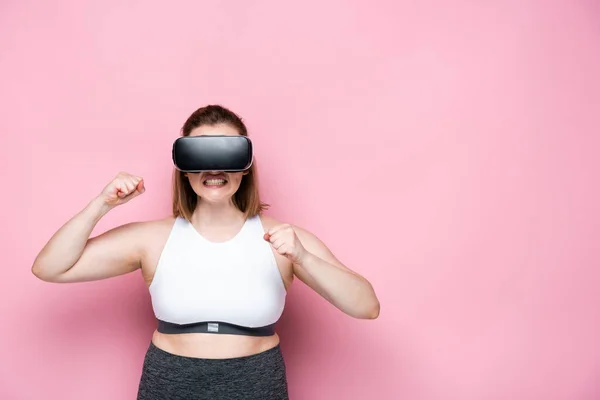 Aggressive overweight girl in sportswear and vr headset with clenched fists on pink — Stock Photo