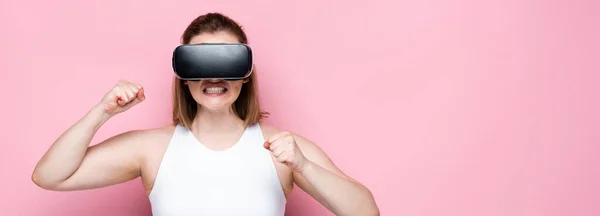Horizontal image of aggressive overweight girl in sportswear and vr headset with clenched fists on pink — Stock Photo