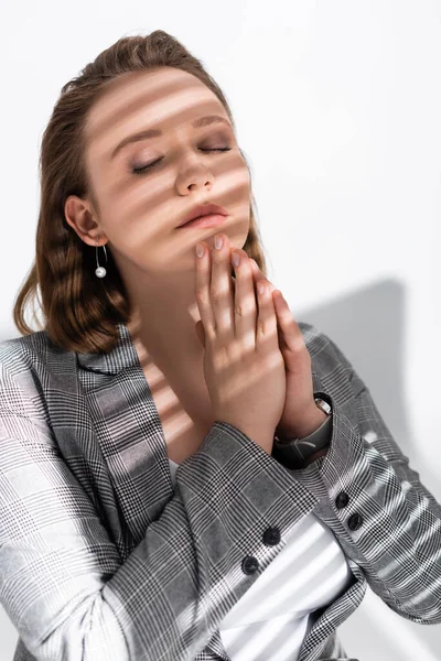 Thoughtful, beautiful overweight girl with closed eyes and praying hands on white in sunlight with shadows — Stock Photo