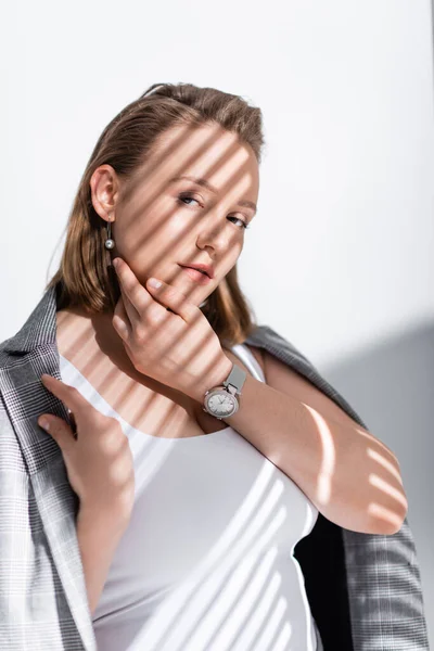 Pensive, confident plus size girl in white top and grey blazer looking at camera on white in sunlight with shadows — Stock Photo