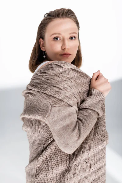 Pretty, serious overweight girl touching wrapping in grey sweater while looking at camera on white with sunlight and shadows — Stock Photo