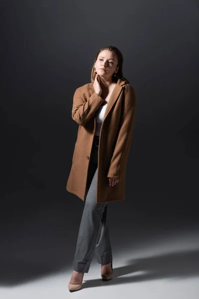 Vista comprimento total da moda plus tamanho menina tocando pescoço enquanto posando em cinza — Fotografia de Stock