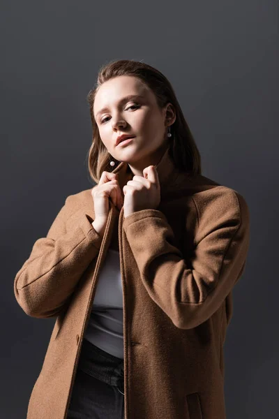 Confident, beautiful overweight girl touching collar while looking at camera isolated on grey — Stock Photo