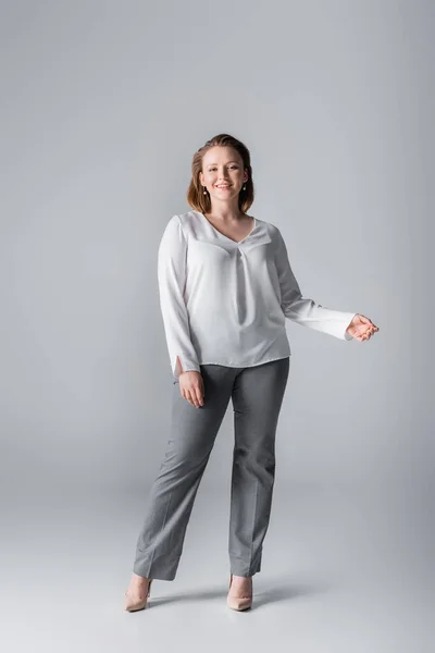 Full length view of stylish overweight girl smiling at camera while posing on grey — Stock Photo