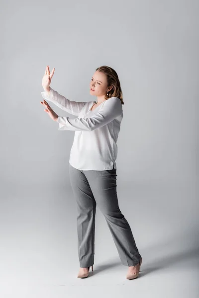 Vista completa de la chica elegante con sobrepeso haciendo gestos con las manos mientras posan en gris - foto de stock