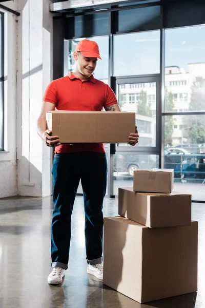 Heureux livreur tenant boîte en carton et regardant les colis — Photo de stock