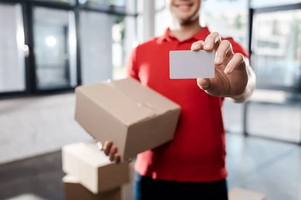 Vue recadrée du livreur heureux tenant la carte blanche et la boîte en carton — Photo de stock