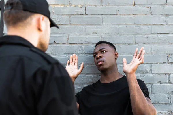 Foco seletivo do homem americano africano com as mãos levantadas olhando para o policial, conceito de racismo — Fotografia de Stock