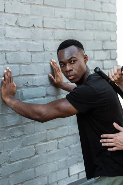 Schöner afrikanisch-amerikanischer Mann steht gegen Ziegelmauer neben Polizist, Rassismus-Konzept — Stockfoto