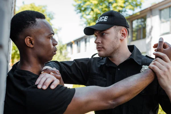 Policía en uniforme que detiene al hombre afroamericano en la calle, concepto de racismo - foto de stock