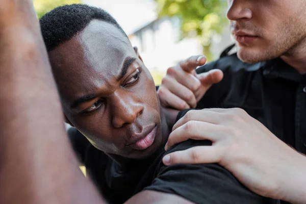 Enfoque selectivo de policía que detiene a hombre afroamericano en la calle, concepto de racismo - foto de stock