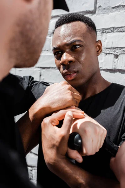 Agente di polizia in possesso di manganello di polizia vicino all'uomo afroamericano, concetto di razzismo — Foto stock