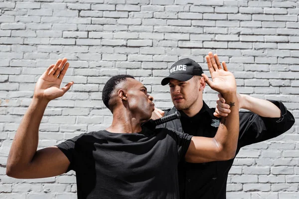 Policeman with baton detaining african american man with raised hands, racism concept — Stock Photo
