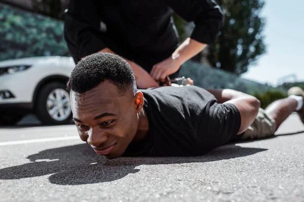 Вибірковий фокус затриманого афроамериканця, який лежить на вулиці біля поліцейського, концепція расизму — стокове фото