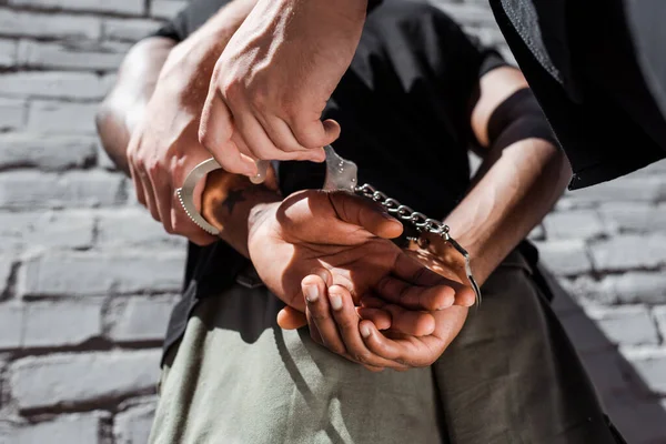 Vue recadrée d'un policier touchant un homme afro-américain menotté — Photo de stock