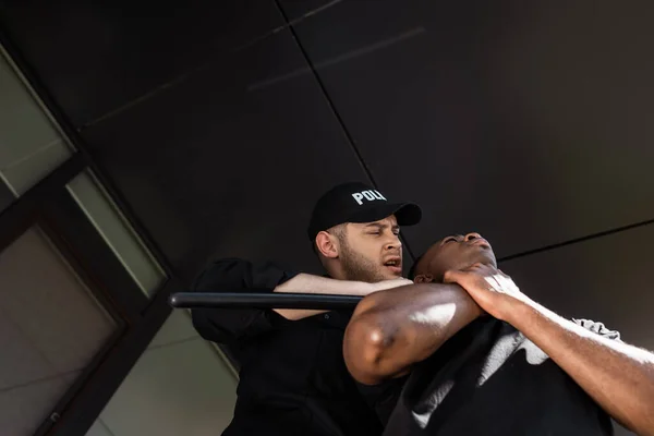 Vue à angle bas d'un policier tenant une matraque près d'un homme afro-américain, concept de racisme — Photo de stock