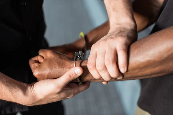 Vista recortada del policía tocando la mano del hombre afroamericano esposado - foto de stock