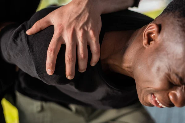 Police officer detaining african american man suffering from pain, racism concept — Stock Photo