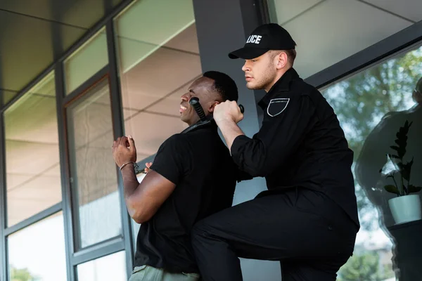 Poliziotto in berretto in possesso di manganello della polizia vicino alla gola di ammanettato uomo africano americano, concetto di razzismo — Foto stock