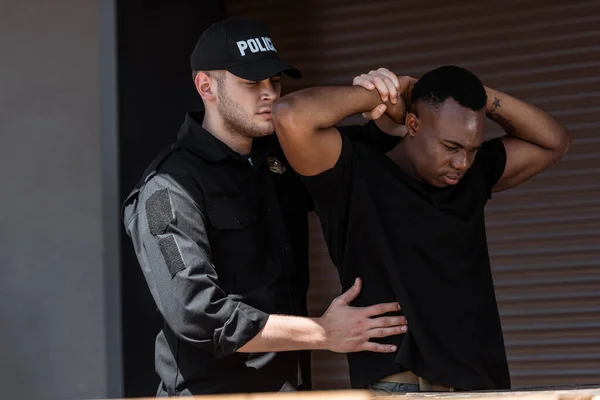 Agente di polizia in berretto con lettere della polizia trattenere l'uomo africano americano — Foto stock