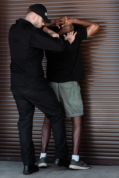 Police officer in uniform and cap arresting african american man — Stock Photo