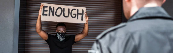 Cultivo horizontal de hombre afroamericano sosteniendo pancarta con suficientes letras cerca de policía, concepto de racismo - foto de stock