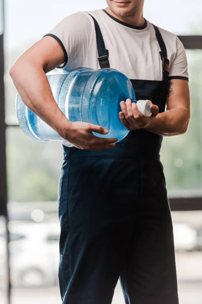 Cropped view of delivery man in uniform holding bottled water — Stock Photo